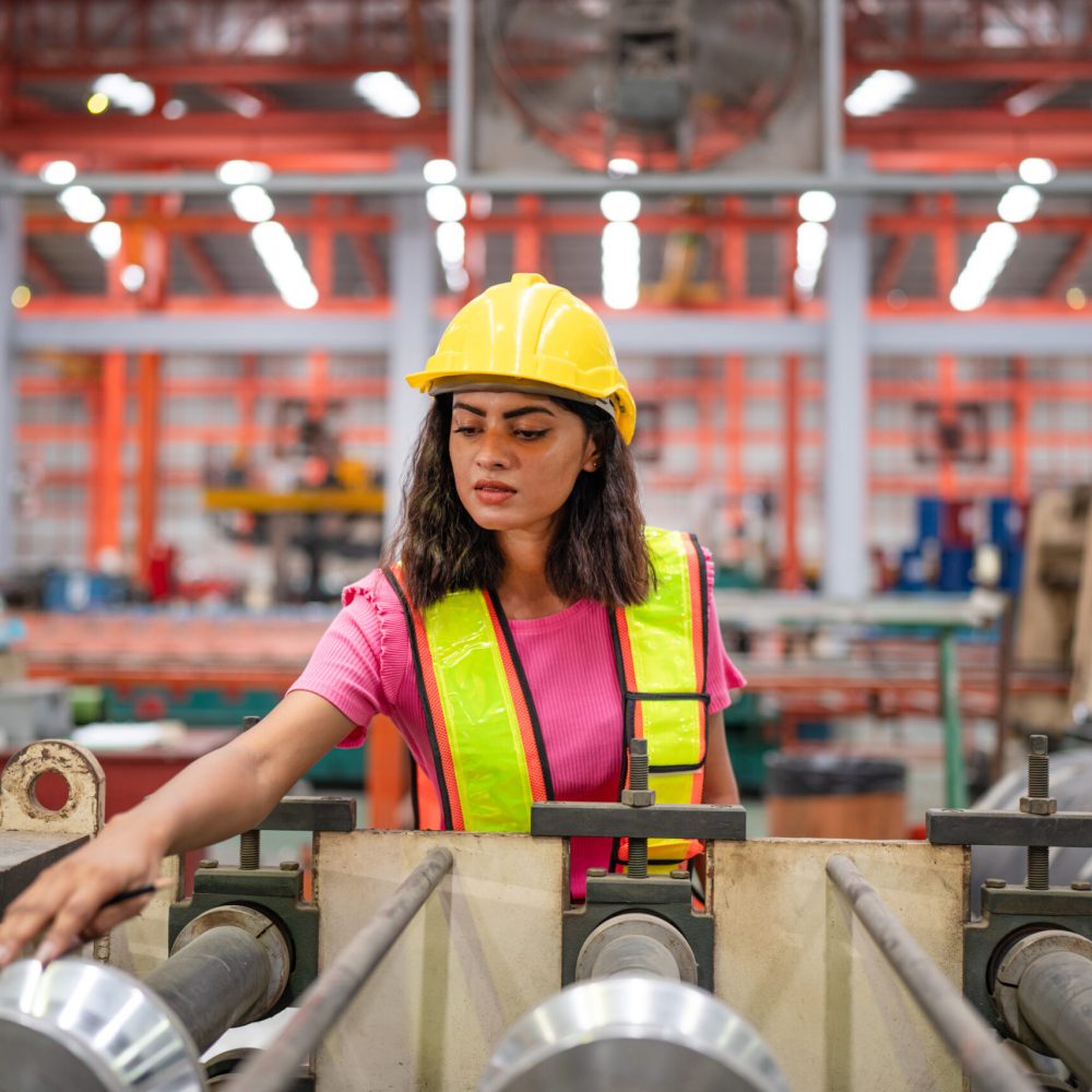 Female industrial engineer or factory worker wearing a yellow helmet working in industrial factory.